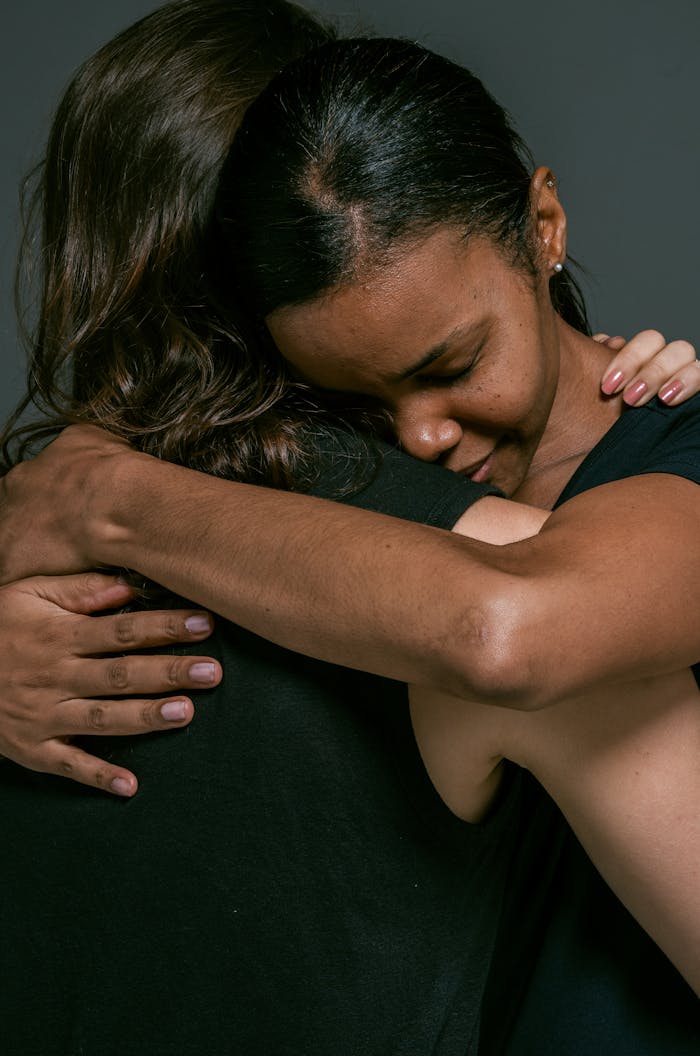 Two women share a heartfelt hug, eyes closed, radiating love and affection.